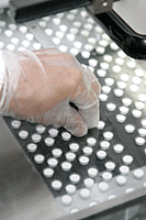 Photo of a gloved hand manufacturing tablets
